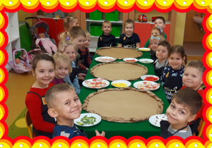 Dzieci siedzą przy stole. Przed nimi kartonowe pizze.